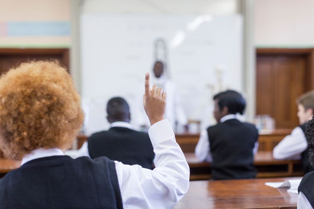 Waist up shot of African male teacher leading biology class, out of focus, students foregrounded with hands up, Cape Town, South Africa