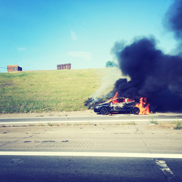 View Of Burning Car On Road Against Clear Sky