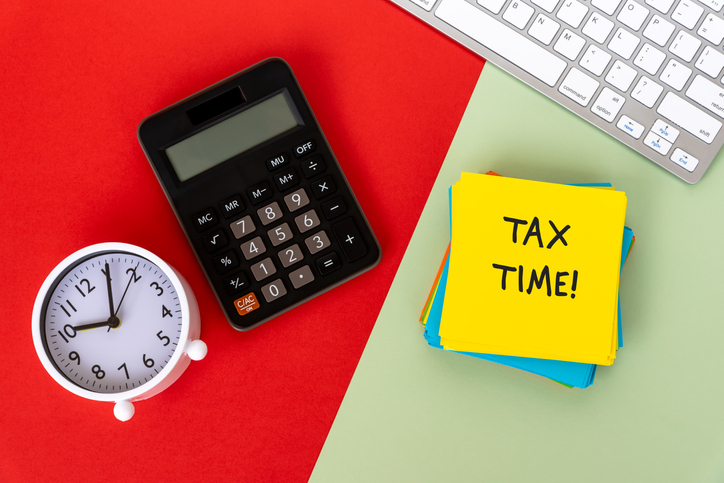 Tax Time on Paper Note With Calculator, Computer Keyboard and Alarm Clock On Red and Green Background