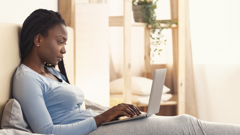 African American Girl Using Laptop Working Sitting In Bed, Panorama