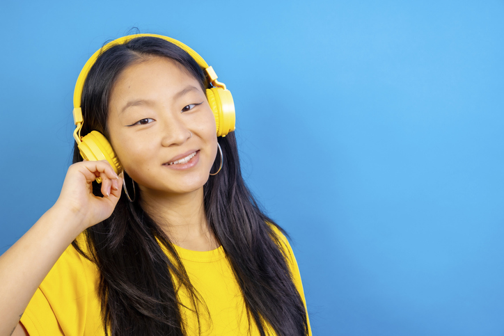 Studio photo with blue background of a chinese woman using headphones smiling at camera