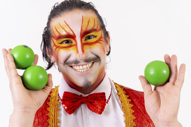 Portrait of smiling juggler juggling green balls isolated on white background