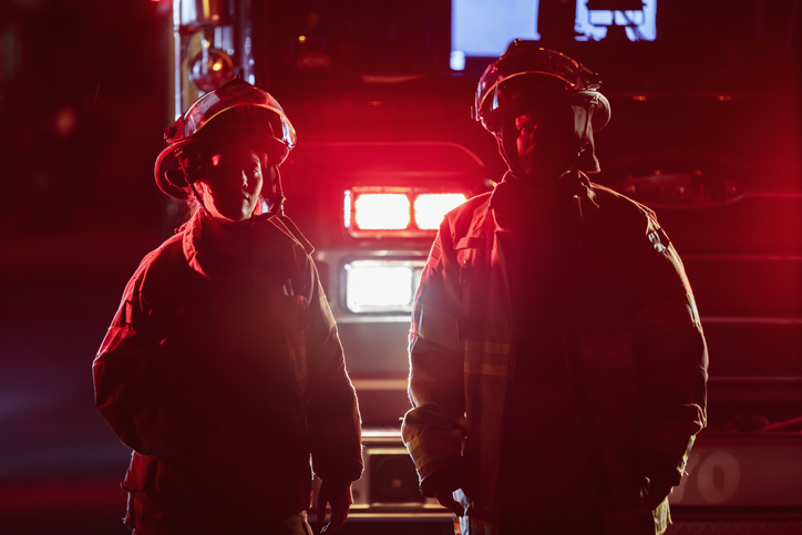 Silhouette of two multiracial firefighters with firetruck at night